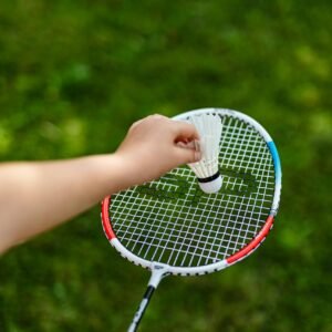 A hand places a shuttlecock on a badminton racket in an outdoor grassy setting.